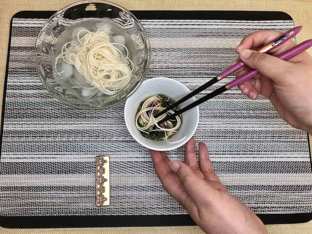 somen served over ice with a person dipping some of the noodles in sauce