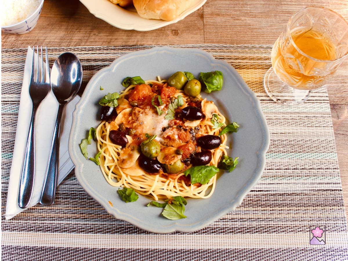 Delicious Spaghetti and Puttanesca Sauce served on a flower shaped ceramic plate with a glass of cold green tea.