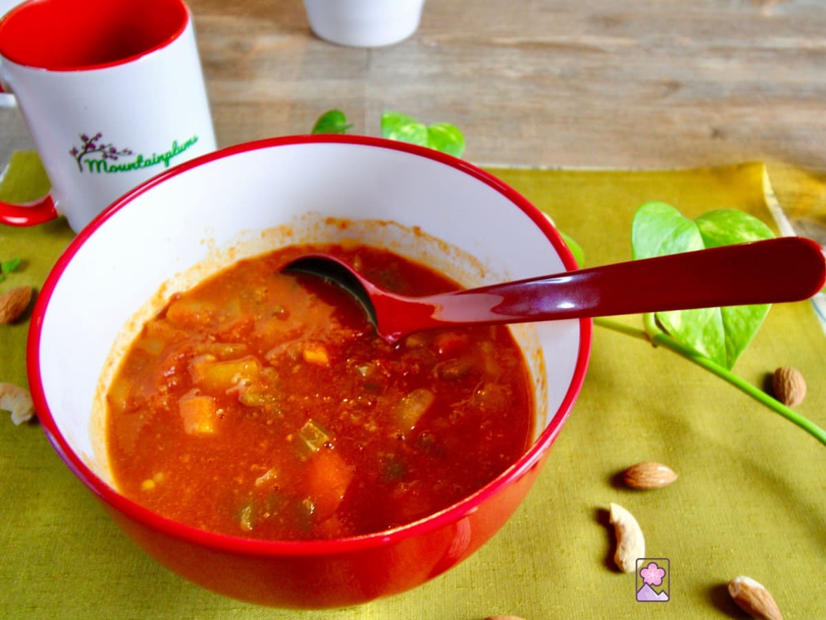 A red, chunky in a Japanese bowl sitting on a green placemat on top of a wooden table. There is a mountain plums cup in the background