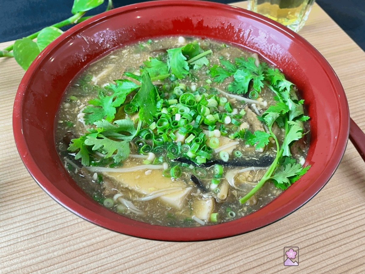Fragrant Hot and Sour Soup served in a red Chinese Soup bowl on a wood table.