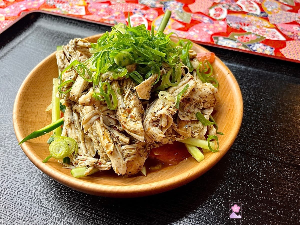 Steamed and shredded chicken mixed with a sauce made with black sesame seed paste. Served in a wooden bowl on a black tray on paper with Chinese patterns.