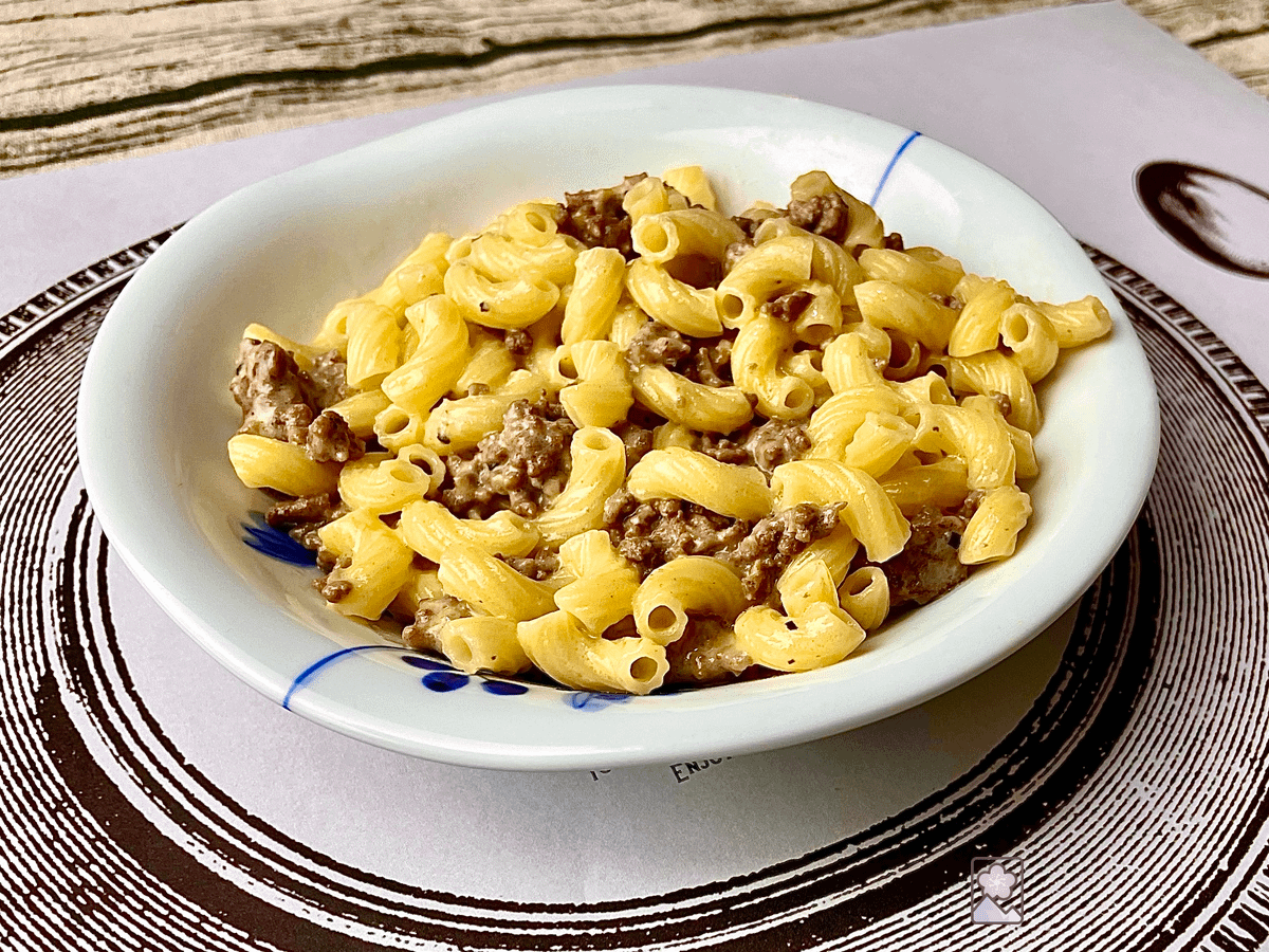 Macaroni and cheese loaded with browned ground beef and melted cheese. Served in a white Japanese ceramic bowl on a paper placemat.