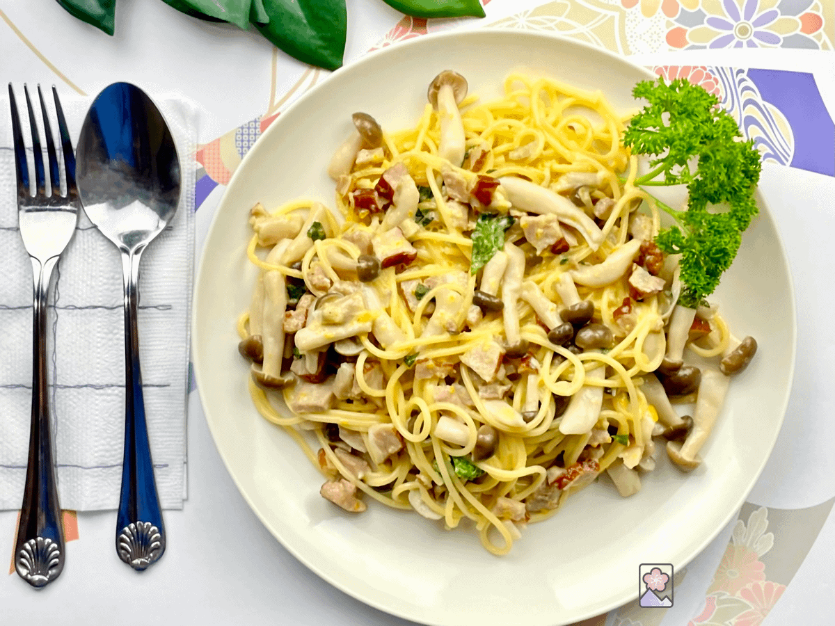 Bacon and Kinoko Pasta on a plate with a spoon and a fork to the left of the plate.