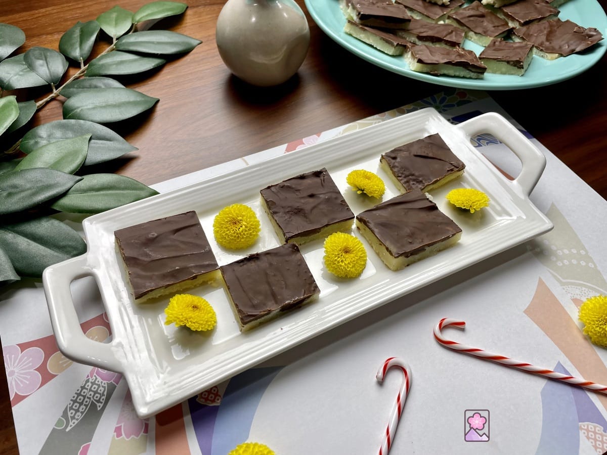 Chocolate Covered Butter Toffees arranged in a checkerboard pattern on a long plate. In the. Background is a second plate with more toffees.