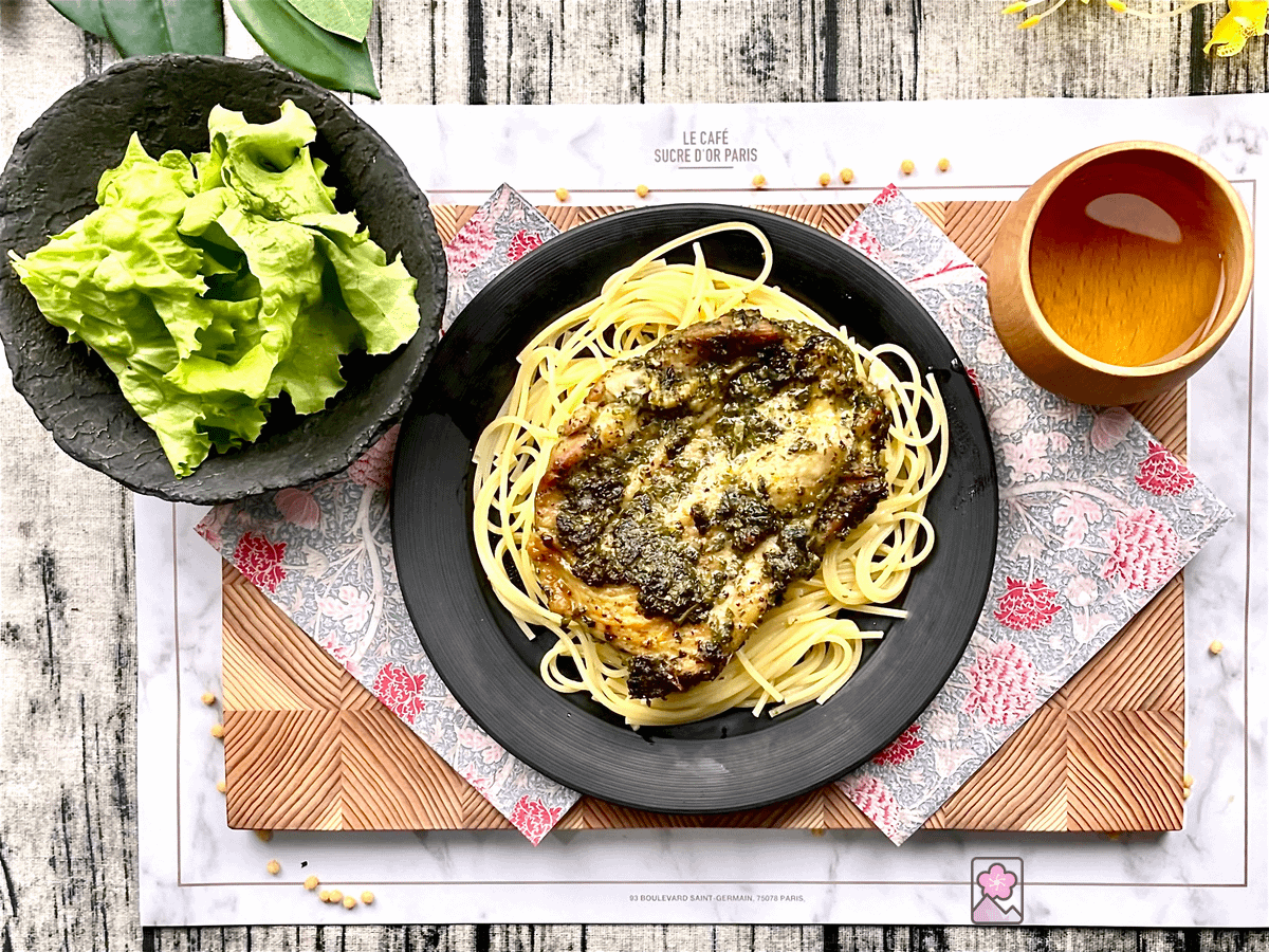 Marinated Basil Chicken on a bed of spaghetti on a ceramic plate. There is a salad and a cup of tea behind it.