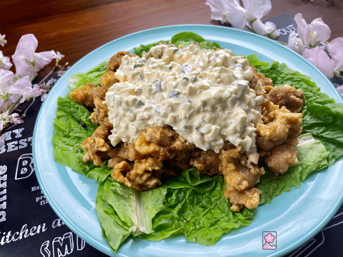 Chicken Nanban on a bed of lettuce on a plate with flowers in the background