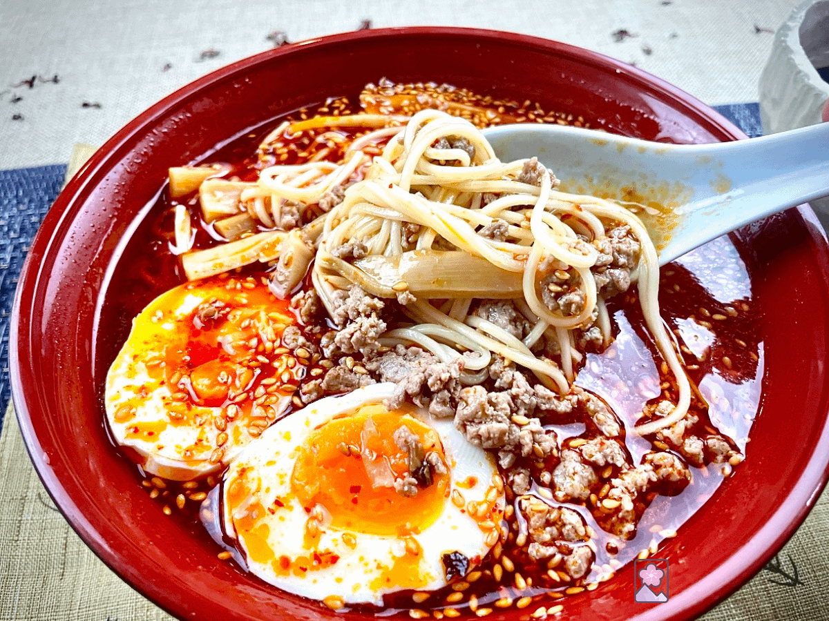 Tantanmen - spicy ramen in soup in a large bowl. Two egg halves with runny yolks, ground pork, and Menma chutes are mixed in and sesame seeds are sprinkled on top.,