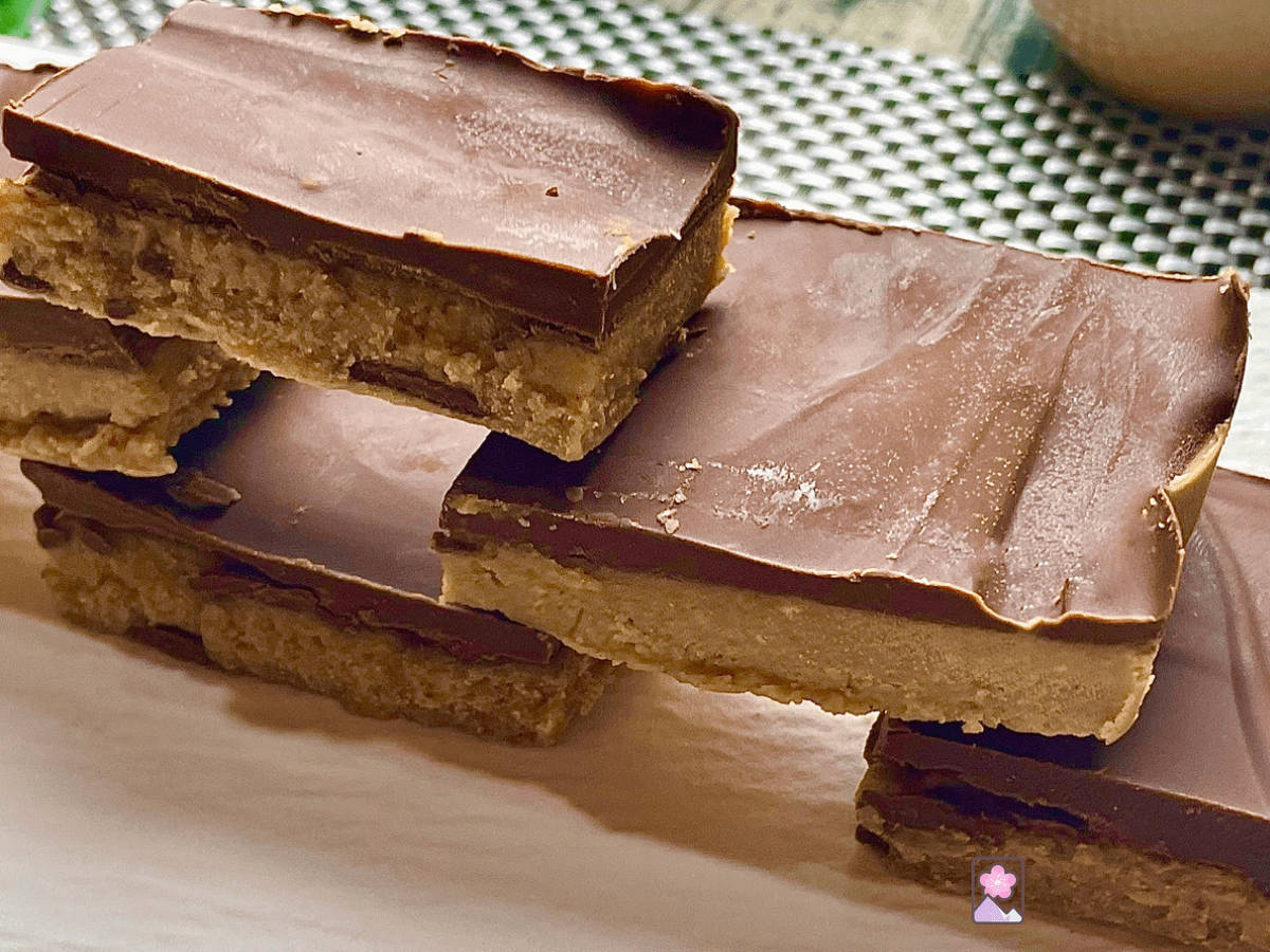 Peanut butter bars with a layer of chocolate on top, stacked on a ceramic plate