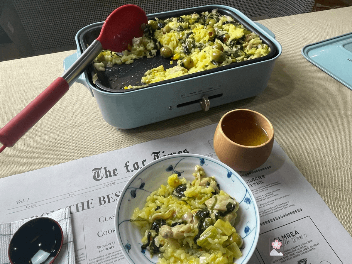 Paella with chicken and olives in a hot plate being served into a ceramic bowl