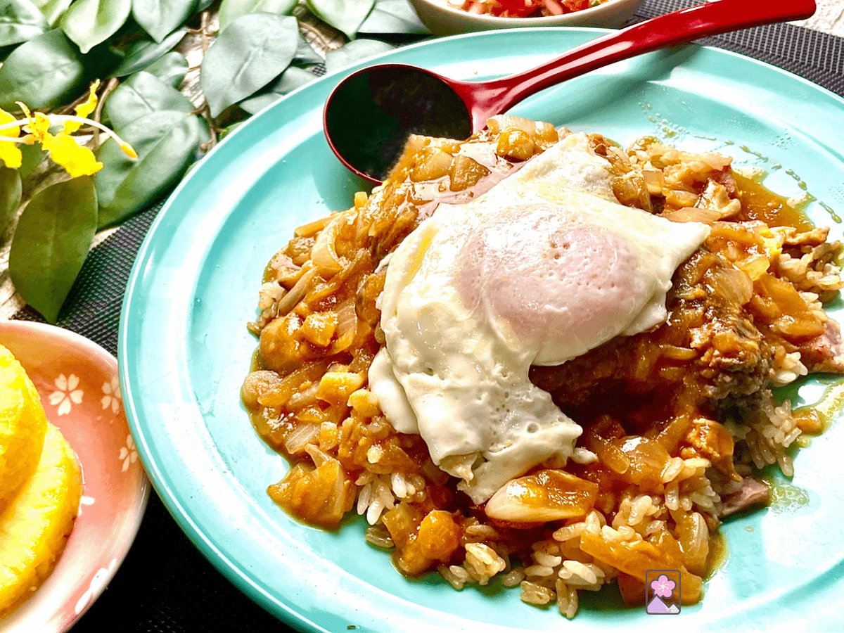 Loco Moco on a large plate with a small,dish of pineapple in the foreground.