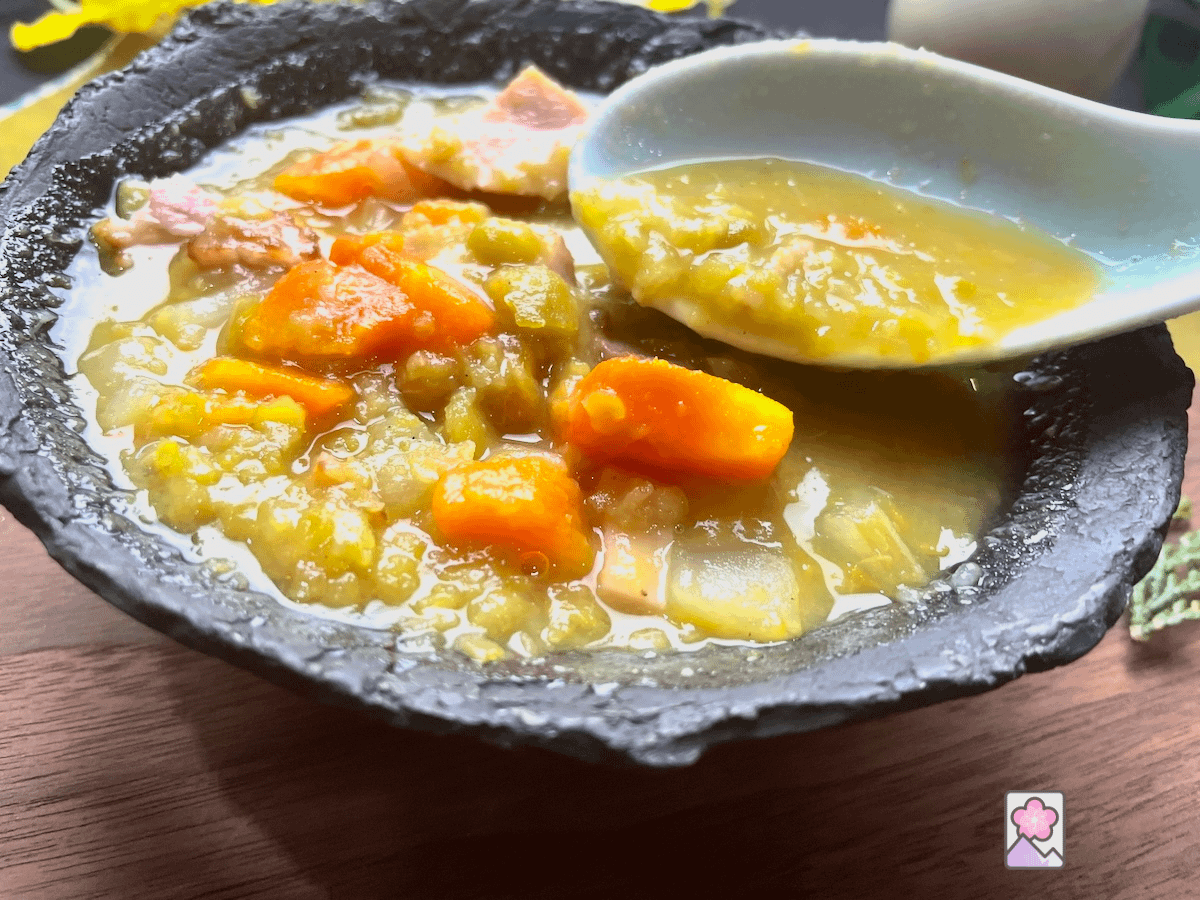 Chunky Split Pea Soup in a black ceramic bowl served on a wooden board. A chunky spoonful of delicious and savory soup is being lifted out of the bowl.