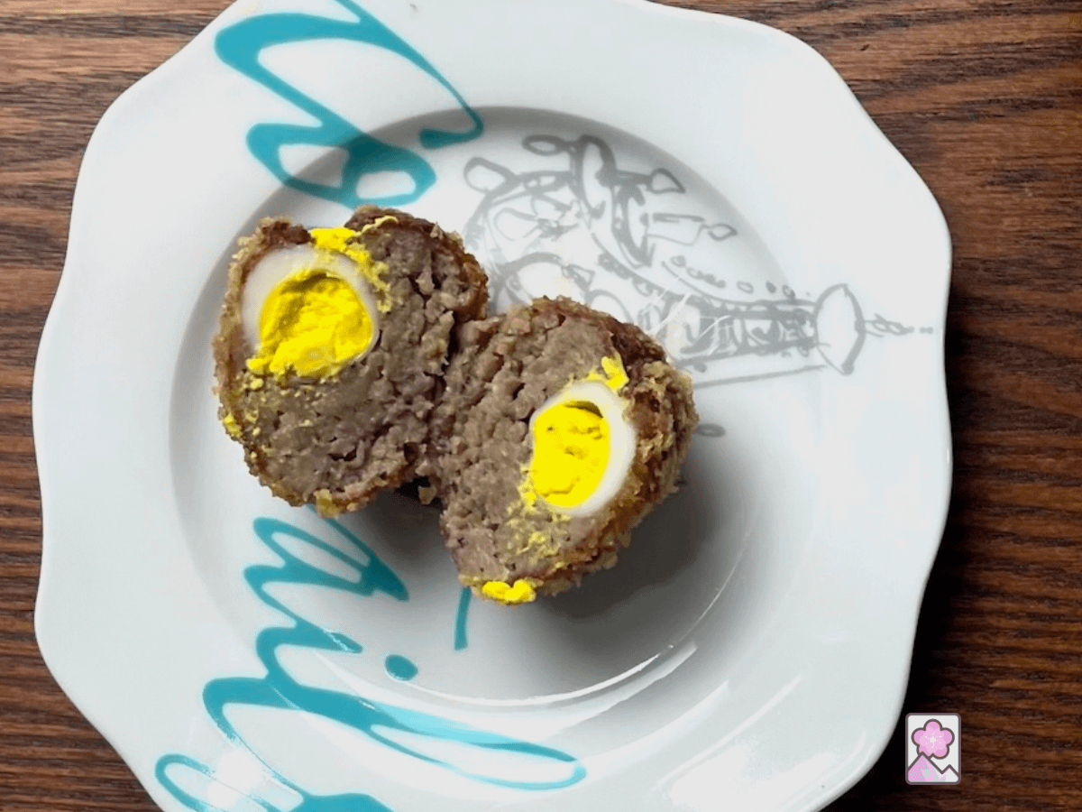 A mini scotch egg sliced in two. The sausage is in a layer surrounding the egg. Both halves are egg side up on a plate.