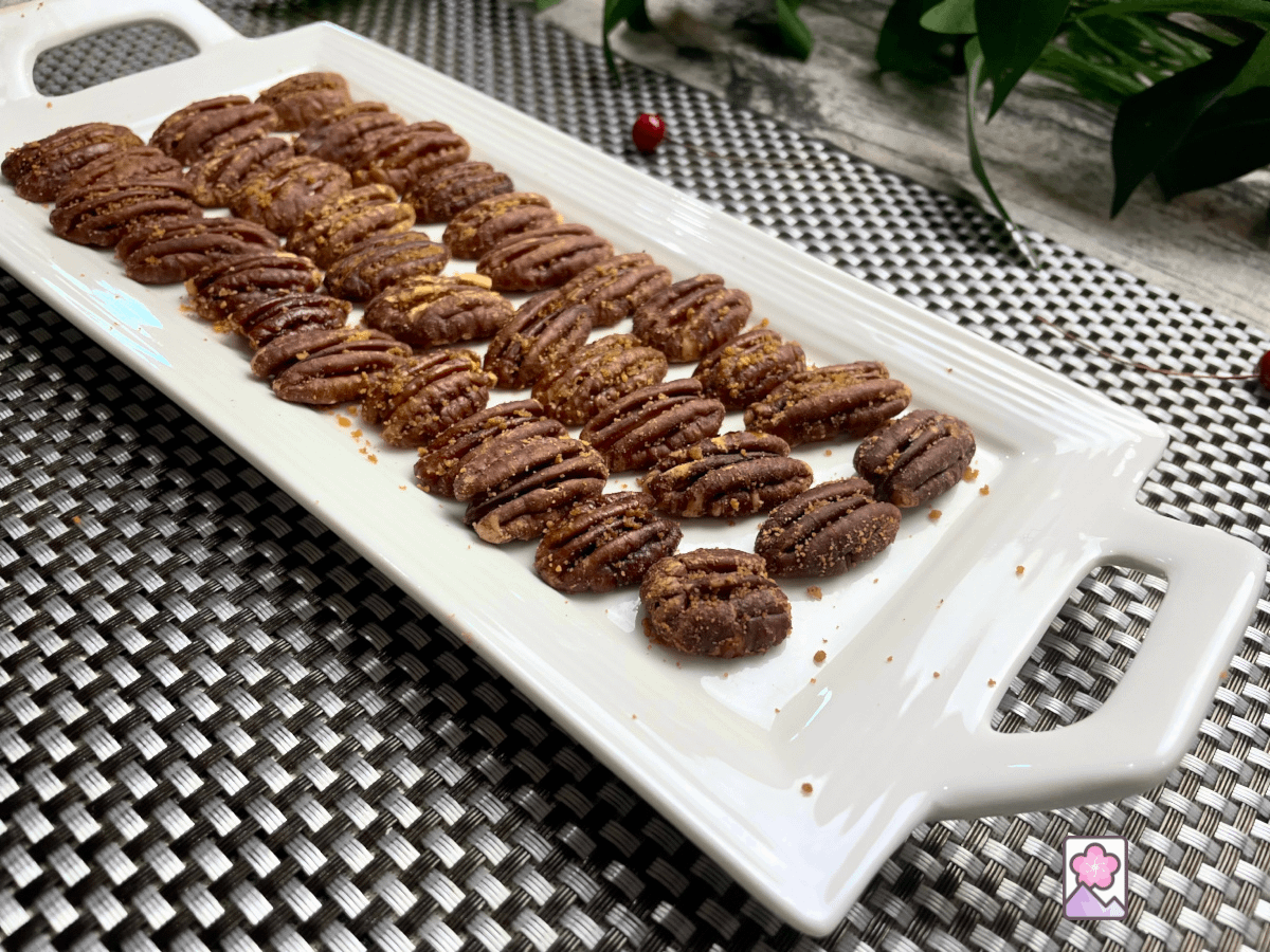 Maple Glazed pecan halves are lined up in three rows on a white tray.
