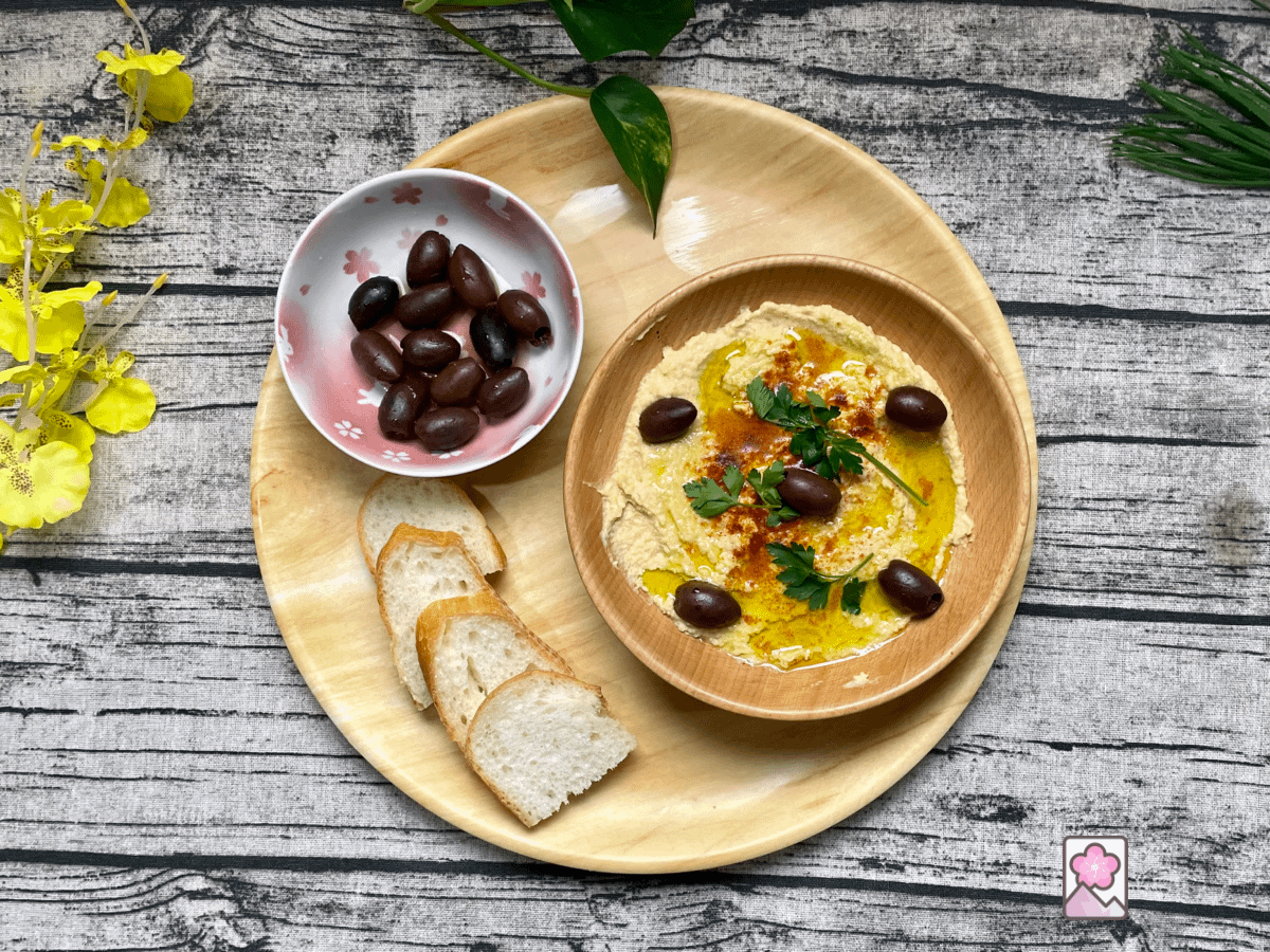 Mediterranean Hummus in a wooden bowl with sliced baguette and olives
