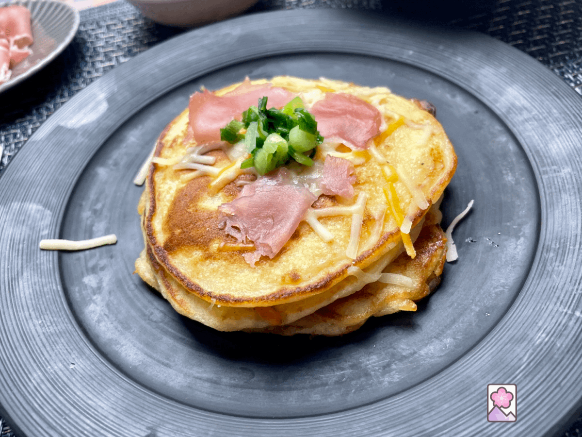 Vichyssoise Potato Pancakes stacked on a plate and sprinkled with shredded cheese and ham