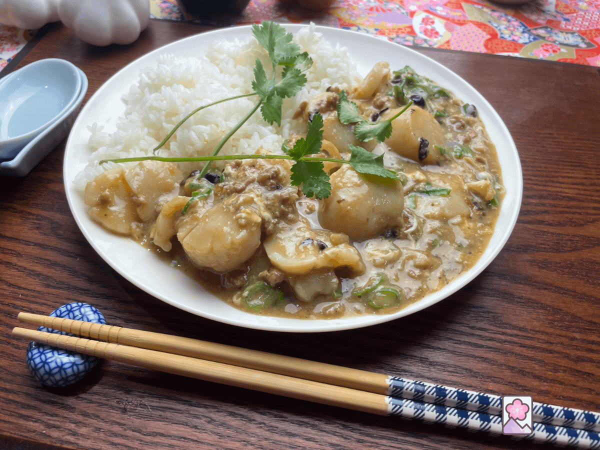 Delicious Scallops in lobster sauce served with white rice and topped with fresh coriander. Served on a round dish with chopsticks in the foreground.