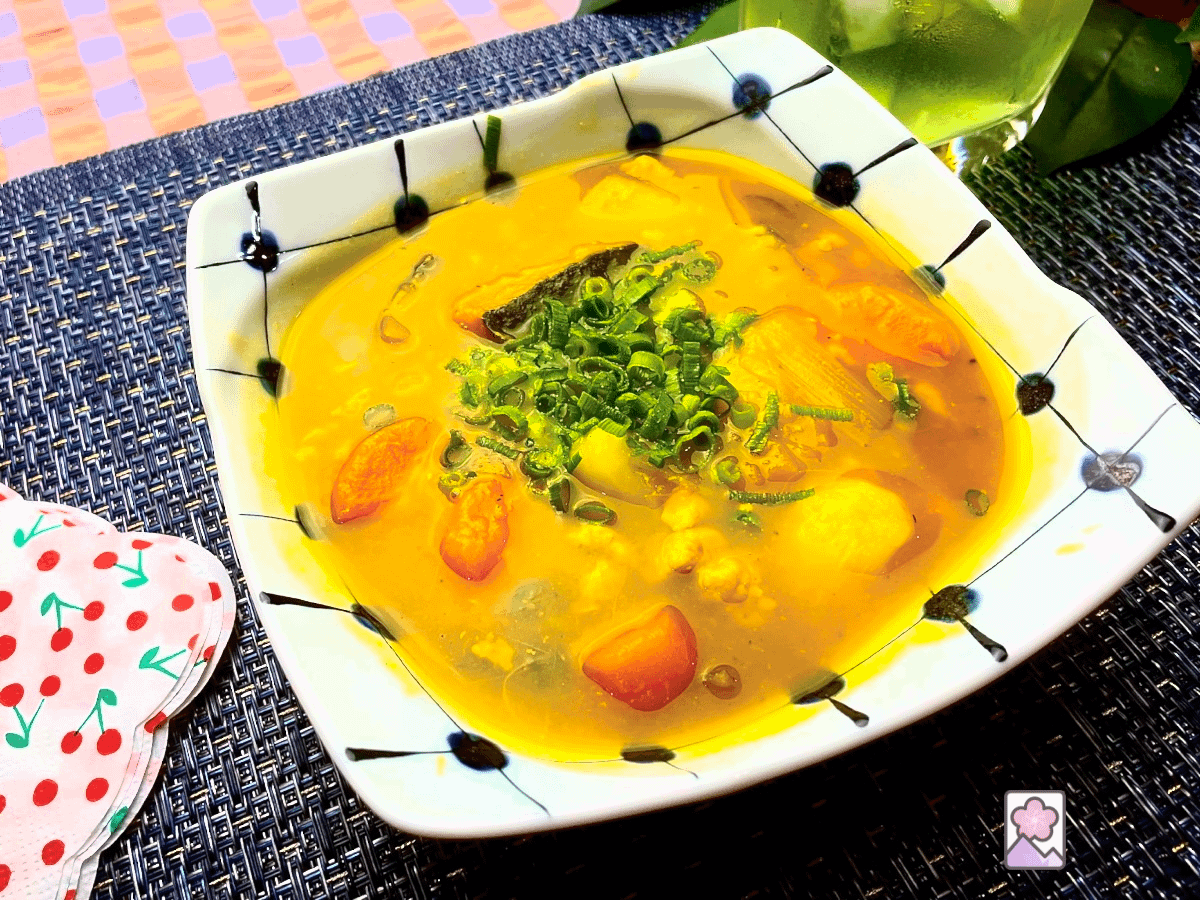 Savory Kabocha Stew in a ceramic bowl topped with chunks of carrot, potatoes and kabocha in a thick stew topped with chopped scallions.