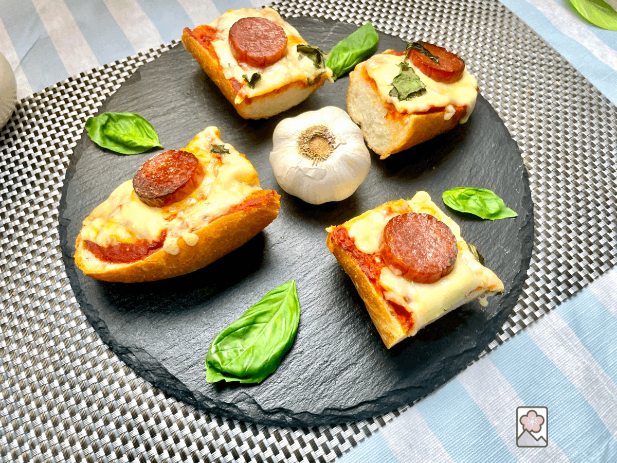 Delicious pizza bread cut in four pieces and placed on a round plate with a fresh basil leaf separating each slice.