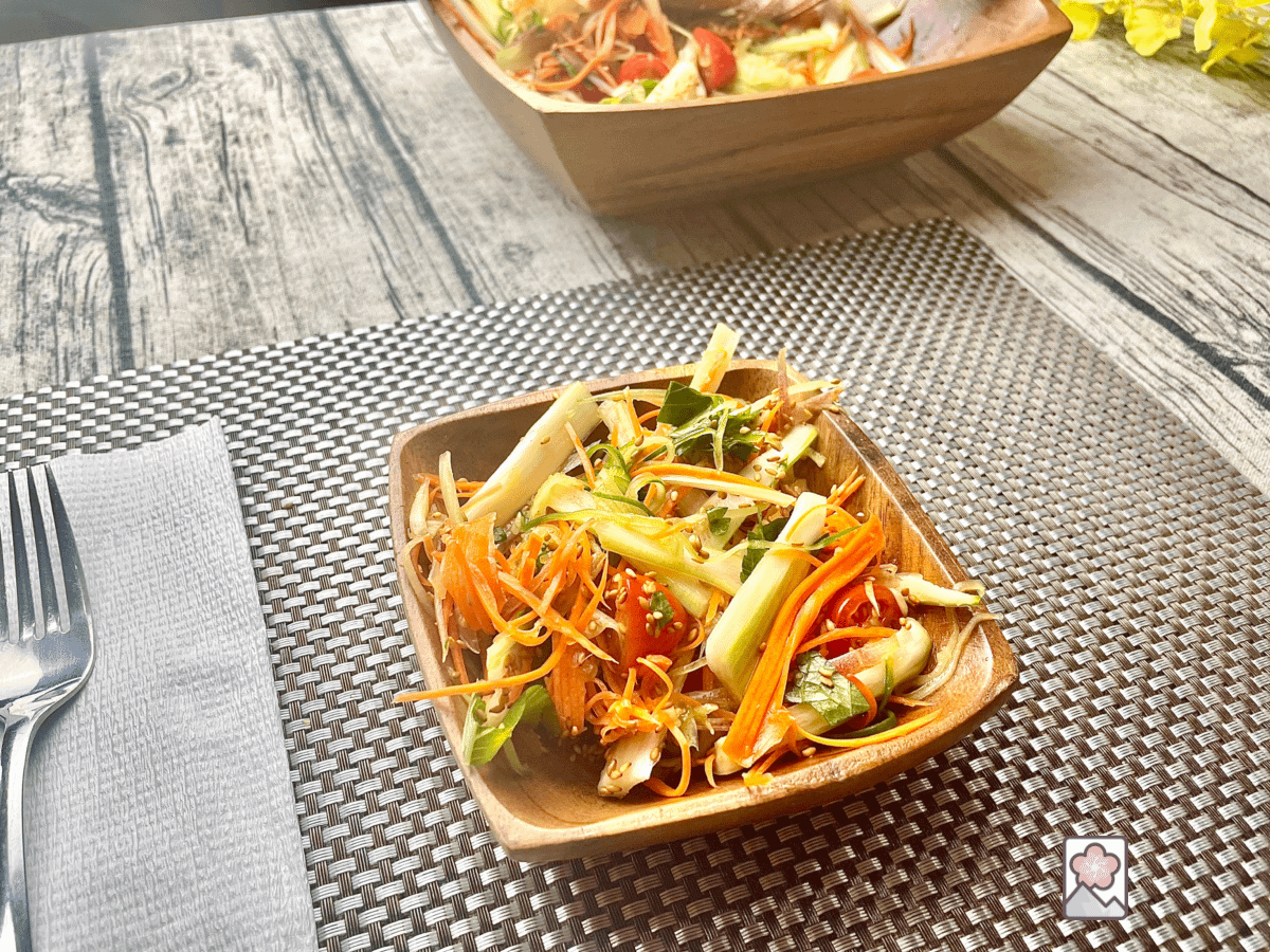 Japanese celery salad served in a wooden salad bowl on a fancy table mat. A wood serving bowl is in the background.