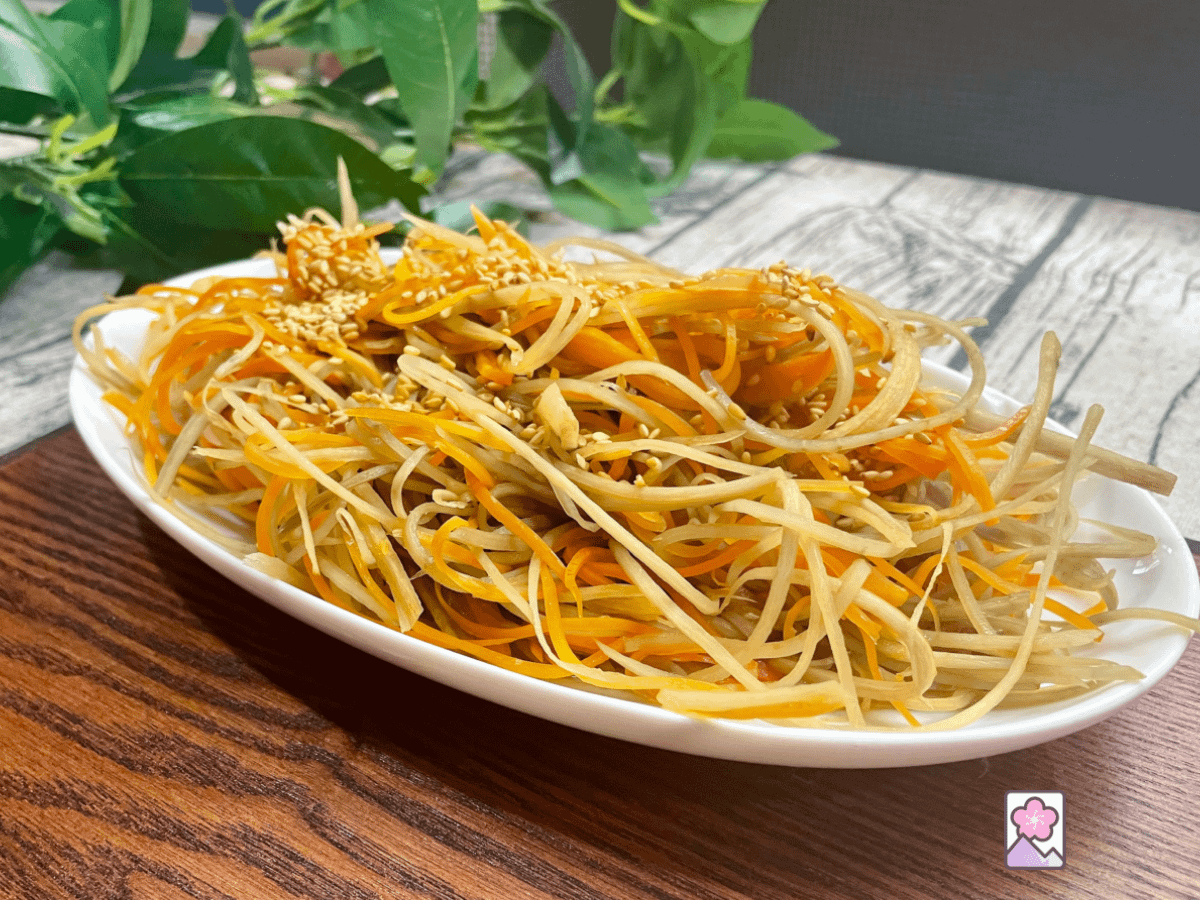 This is my delicious kinpira I made by julienne slicing burdock and carrot and stir frying in a delicious sweet and salty sauce. Topped with toasted sesame seeds and sitting on an oval Japanese plate.