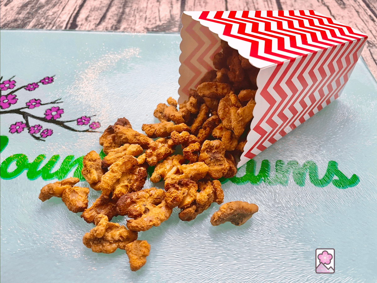 Crunchy Sweet and Spicy Wasabi Coated walnuts spill out of a container onto a colorful glade mountain plums cutting board