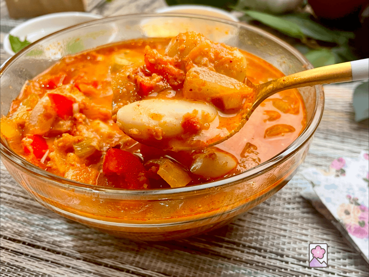Ham and White Bean Chili in a glass bowl, scooped up in a golden spoon. White beans, tomato’s, red pepper permeate the savory and spicy chili.