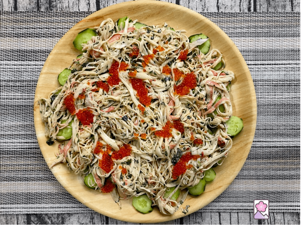 Kani Salad with Mentaiko Dressing sits on a round wooden tray layered with cucumbers, seafood salad, and ikura