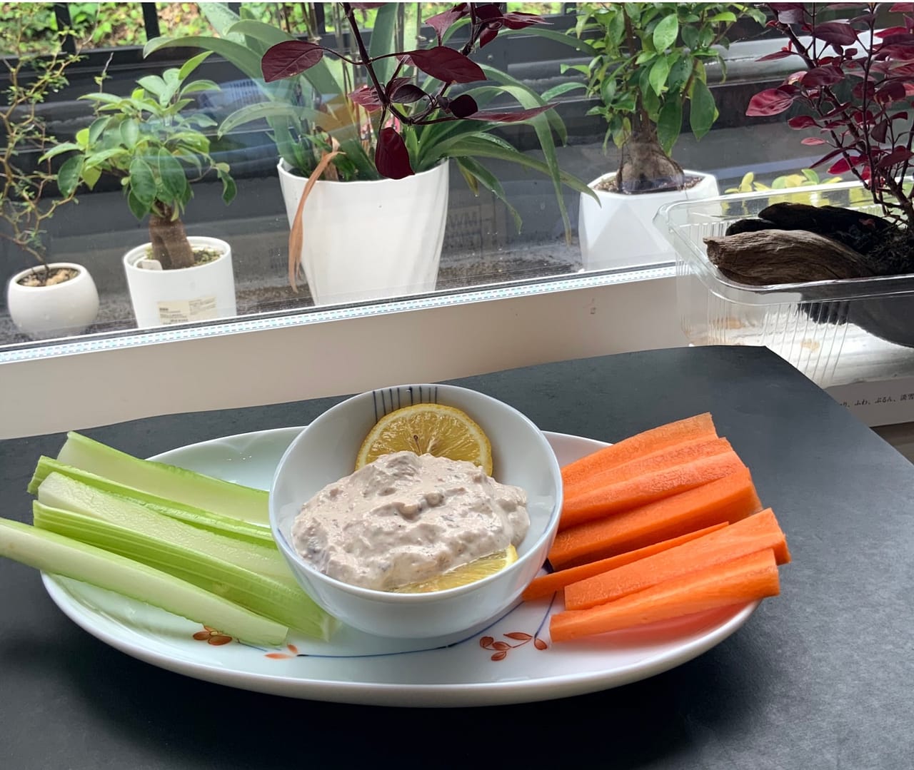 Smoked fish dip is served on an oval plate in a ramekin with carrot and celery sticks on either side.