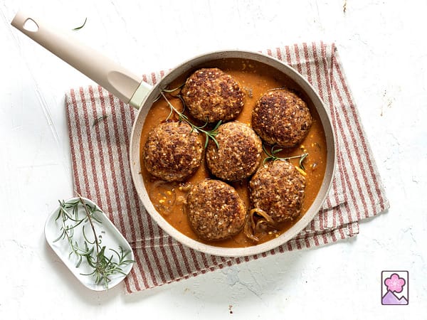 Six Salisbury steaks simmering in sauce in a pan topped with herbs.