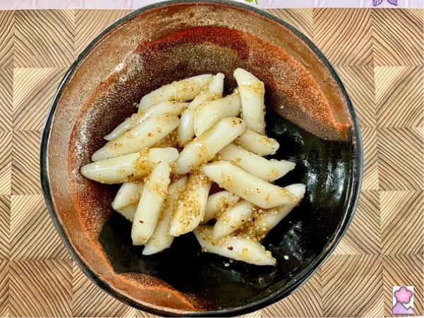 Topokki, cooked with honey and sesame in a ceramic bowl, over a wooden tray.