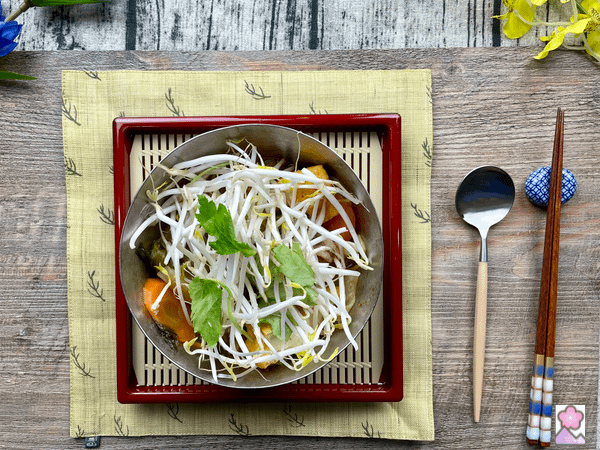 Delicious Kimchi Nabe topped with Mung Beans and Japanese Mitsuba In a steel brown on a bamboo Matt.