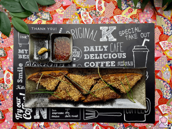 Shrimp toast on a long ceramic plate. The plate is on a trendy placemat on a table with Japanese prints. There are plants in the background.