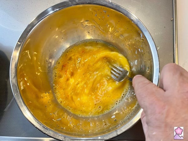 Beating two eggs with a fork in a metal bowl
