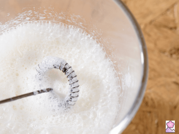 A handheld milk frother is being used in a glass cup to make foam.