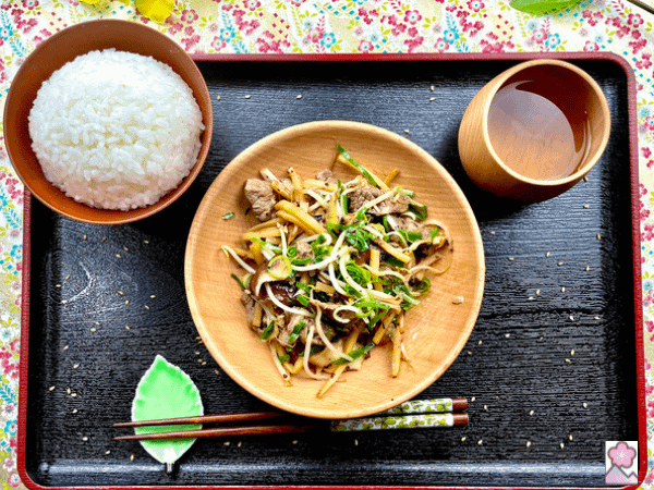 Beef and Bamboo in Black Bean sauce served in a wooden bowl on a tray with white rice and oolong tea in a wooden cup.