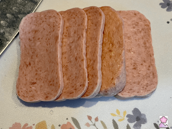 5 slices of spam laid out on a cutting board