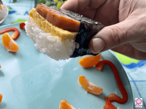 Spam Musubi ready to eat, being held up over a plate