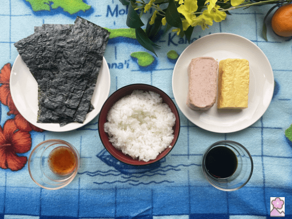 Spam Musubi ingredients- spam, egg, nori, white rice, soy sauce and sweet chili sauce laid out on a map of Hawaii