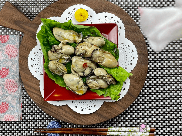 Smokey Marinated Oysters on a round wooden cutting board over a lettuce leaf With a pink flower in the foreground