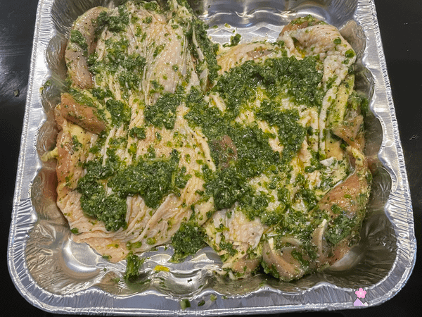 Chicken in a foil pan covered with basil paste and ready to bale
