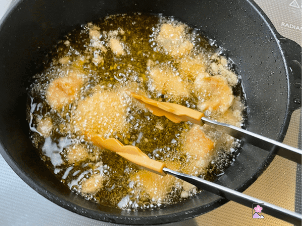 Coated salmon frying in oil in a black pan