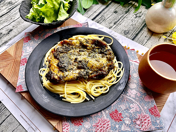 Marinated Basil Chicken over Spaghetti On a black ceramic plate with a simple green salad in the background.