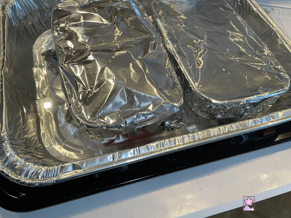 Two terrines in a baking pan in a boiling water bath. The terrines are covered with foil..