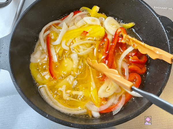 Thin sliced onion and pepper frying in cooking oil in a black pan