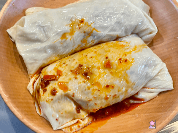 Yuba rolls with sauce being spread over the top in a wooden bowl