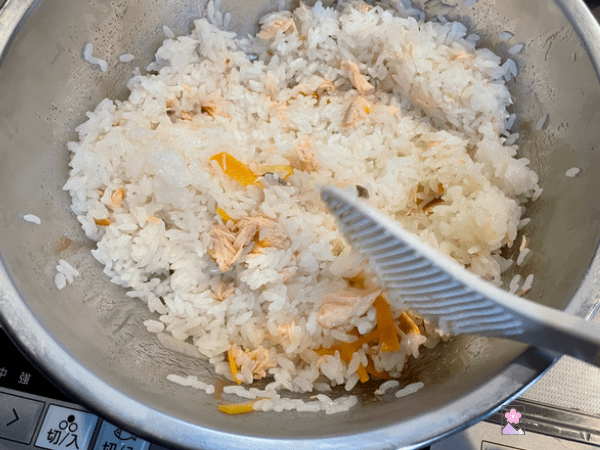 Sushi rice and salmon in a bowl being stirred by a plastic rice spoon