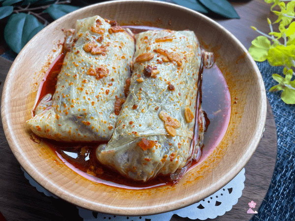 Steamed Yuya rolls served in a wooden bowl and topped with sweet chili sauce