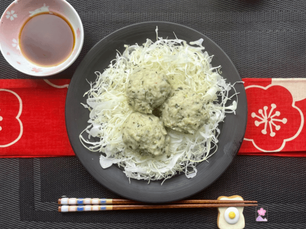 Steamed meatballs on a bed of cabbage on a plate with sauce in a dipping bowl in the background