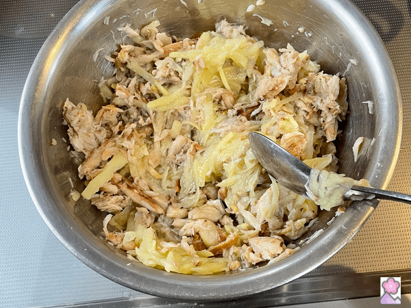 Mixing crabmeat and shredded potatoes in a metal bowl