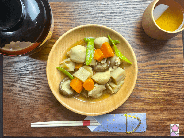 Chicken and Root Vegetable Nimono served on a wooden tray with a teacup, a soup bowl with the lid on, and decorative chopsticks